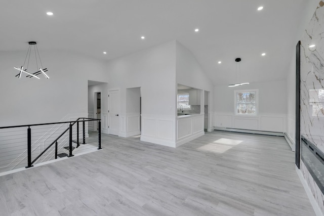 unfurnished living room with sink, light hardwood / wood-style flooring, high vaulted ceiling, baseboard heating, and a chandelier