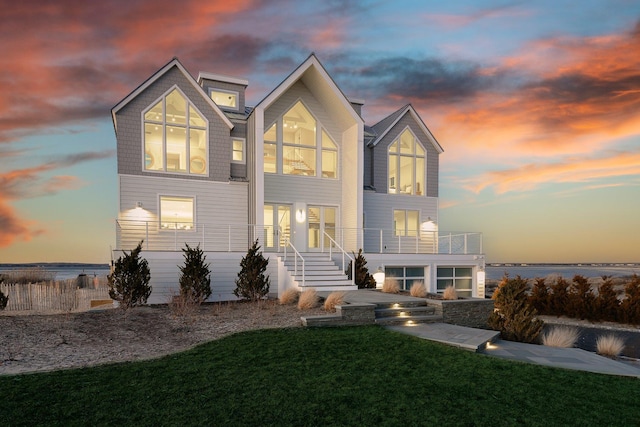 back house at dusk with a balcony, a yard, and a water view