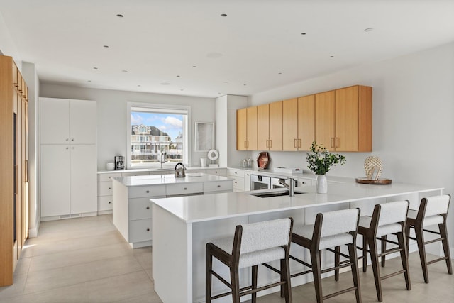 kitchen with kitchen peninsula, light brown cabinets, a kitchen island, white cabinetry, and sink