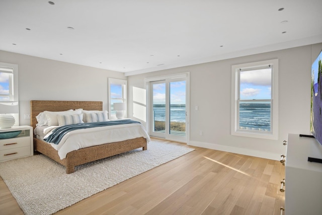 bedroom featuring access to exterior, light hardwood / wood-style floors, and a water view