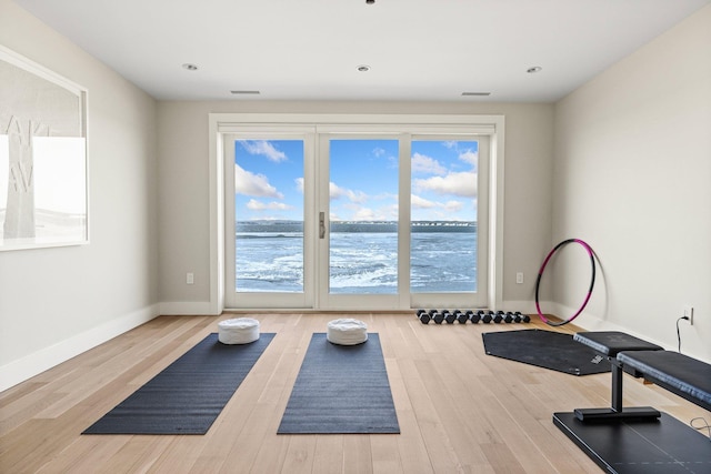 exercise room with a healthy amount of sunlight, a water view, and wood-type flooring