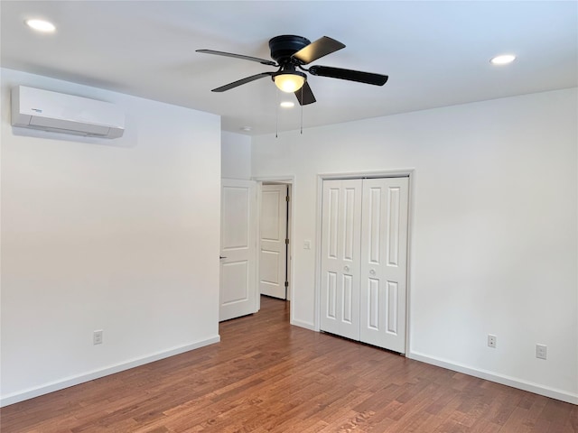 unfurnished bedroom with ceiling fan, hardwood / wood-style floors, a closet, and a wall unit AC