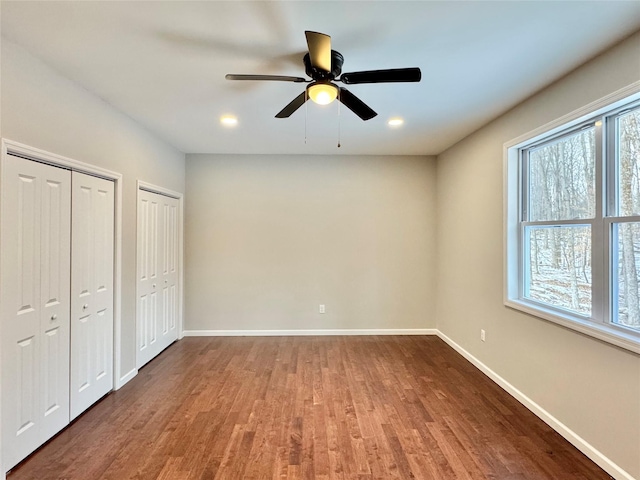 unfurnished bedroom featuring ceiling fan, hardwood / wood-style floors, and two closets