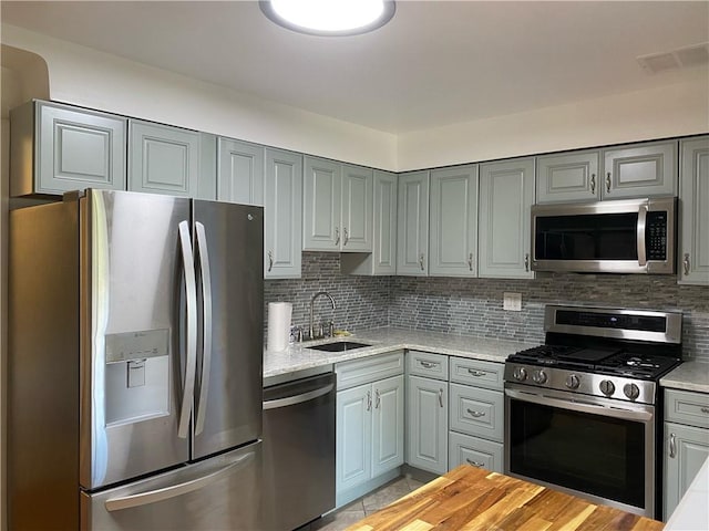 kitchen featuring sink, stainless steel appliances, light stone counters, and tasteful backsplash