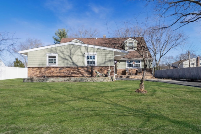 view of front facade with stone siding, a front yard, and fence