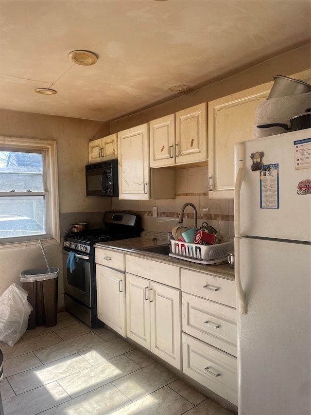 kitchen with dark countertops, freestanding refrigerator, black microwave, a sink, and gas stove