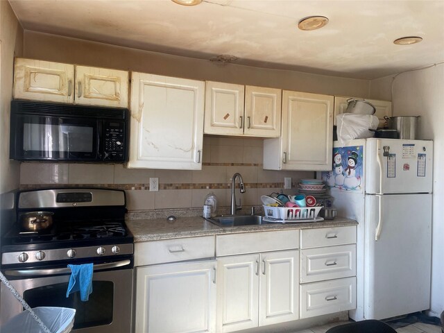 kitchen with tasteful backsplash, freestanding refrigerator, a sink, black microwave, and stainless steel gas range oven