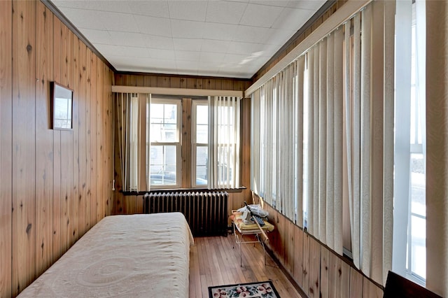 bedroom with wood walls, light wood-type flooring, and radiator