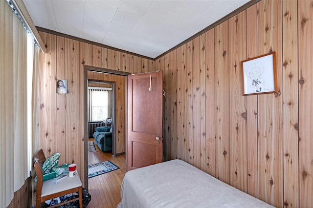 bedroom with crown molding, wooden walls, and wood-type flooring