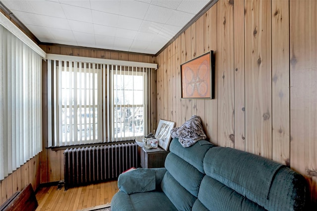 living room with wood-type flooring, radiator, crown molding, and wooden walls