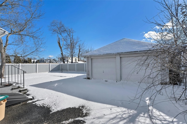 yard layered in snow featuring a garage and an outbuilding