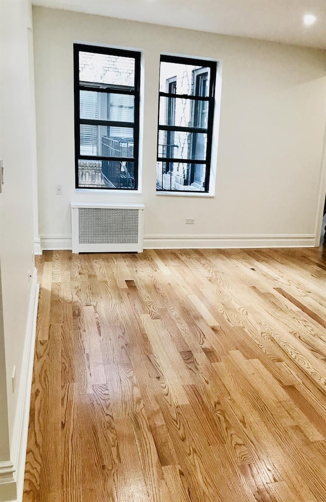 empty room featuring light wood-type flooring, radiator heating unit, and a wealth of natural light