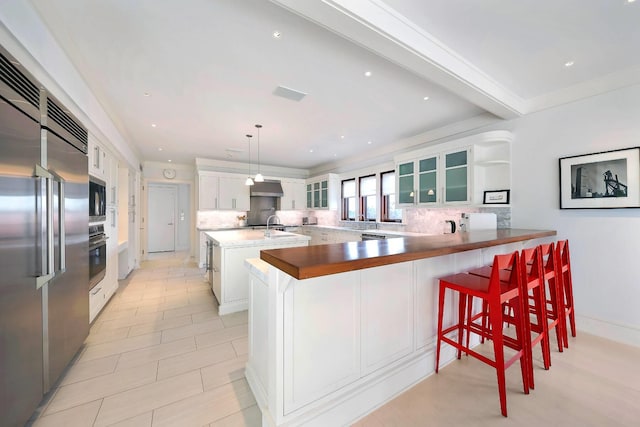 kitchen with pendant lighting, a breakfast bar, kitchen peninsula, built in appliances, and white cabinetry