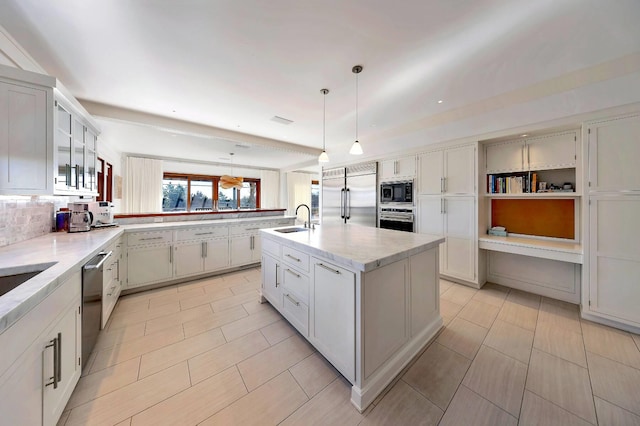 kitchen featuring a center island with sink, pendant lighting, light tile patterned flooring, sink, and built in appliances