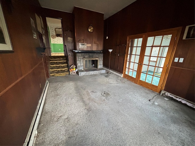 unfurnished living room featuring carpet flooring, wood walls, baseboard heating, and a stone fireplace