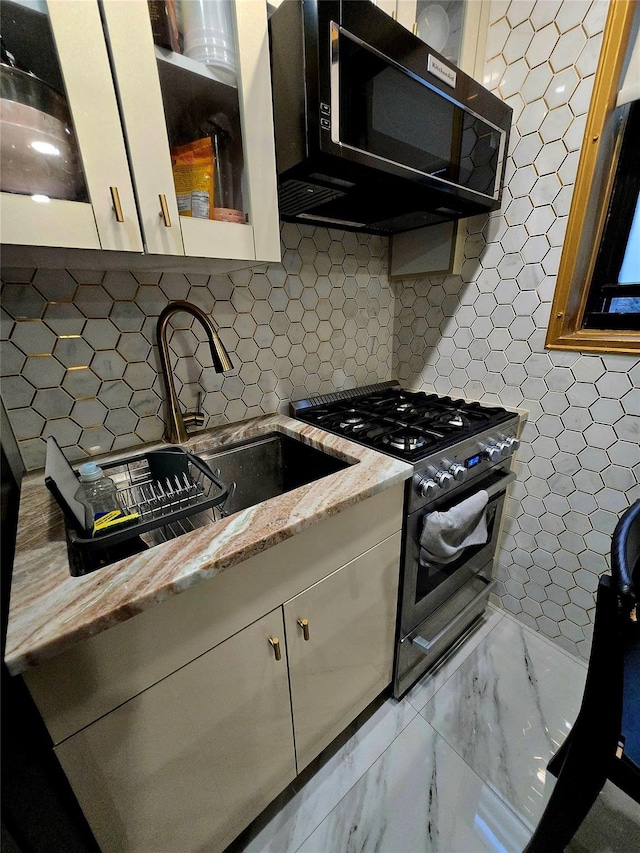 kitchen with white cabinets, backsplash, stainless steel gas stove, and light stone counters