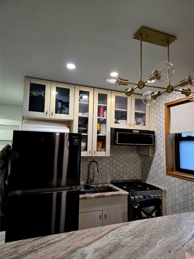 kitchen with white cabinetry, ventilation hood, gas stove, black fridge, and sink