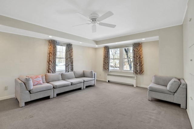 carpeted living room featuring radiator, a raised ceiling, a healthy amount of sunlight, and ceiling fan