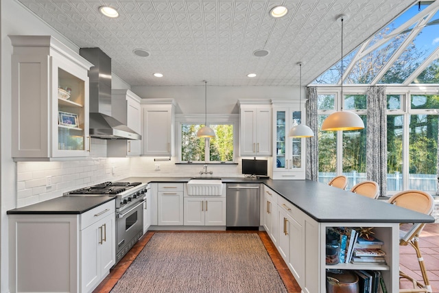 kitchen with wall chimney range hood, pendant lighting, a kitchen bar, white cabinetry, and stainless steel appliances