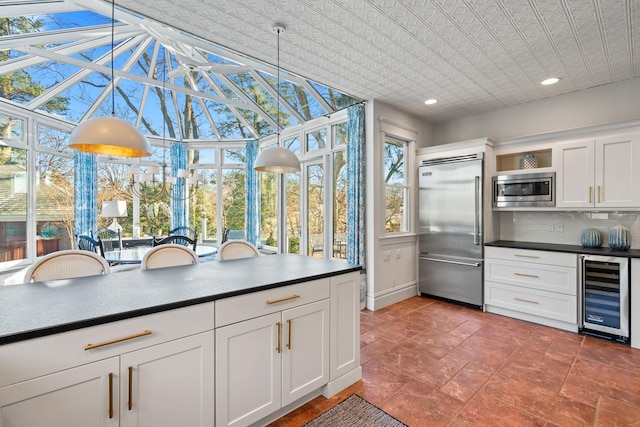 kitchen with decorative backsplash, wine cooler, built in appliances, pendant lighting, and white cabinets