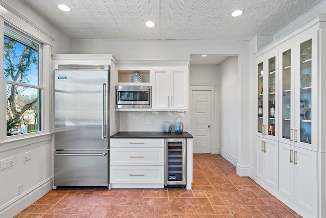 kitchen with decorative backsplash, beverage cooler, white cabinets, and built in appliances