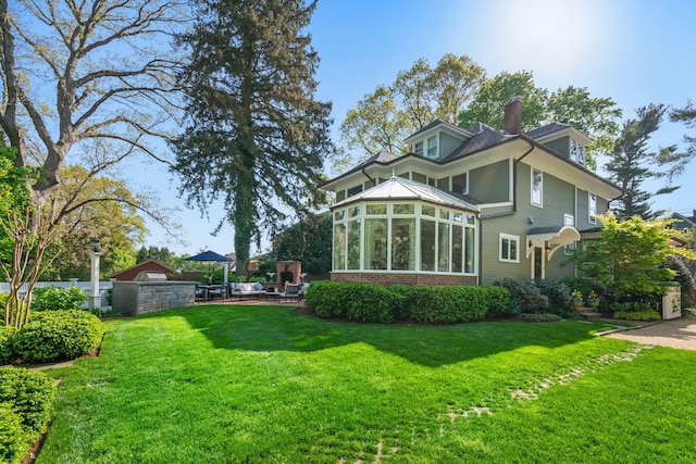 back of property featuring a sunroom, a lawn, a chimney, and brick siding