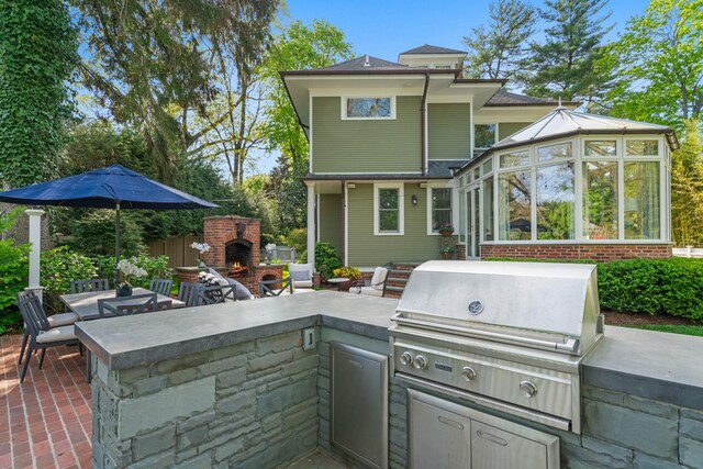 view of patio / terrace with an outdoor kitchen, an outdoor brick fireplace, grilling area, and a sunroom