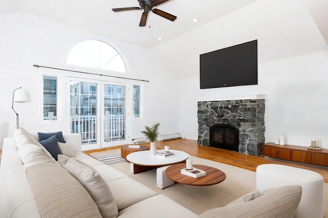 living room featuring ceiling fan, hardwood / wood-style flooring, a stone fireplace, and high vaulted ceiling