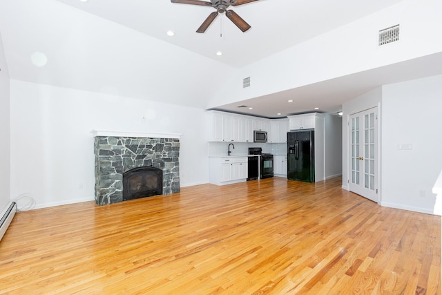 unfurnished living room featuring lofted ceiling, a stone fireplace, light hardwood / wood-style floors, sink, and ceiling fan