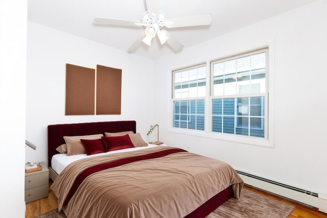 bedroom with ceiling fan, a baseboard heating unit, and hardwood / wood-style flooring