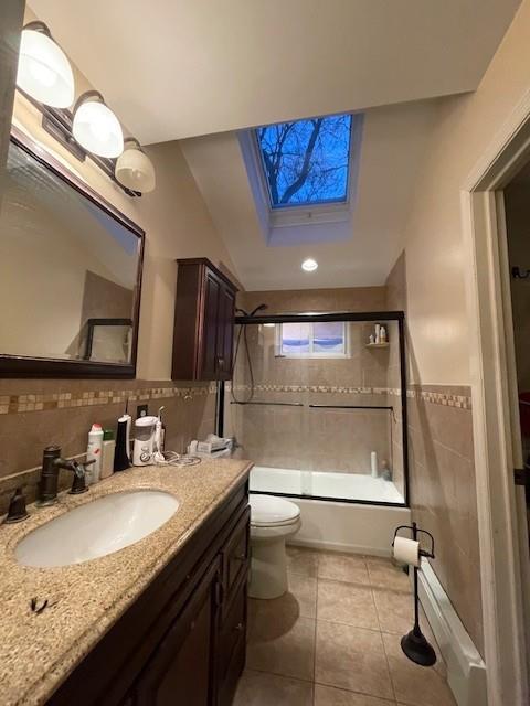 full bathroom featuring tile patterned floors, toilet, shower / bath combination with glass door, a skylight, and vanity