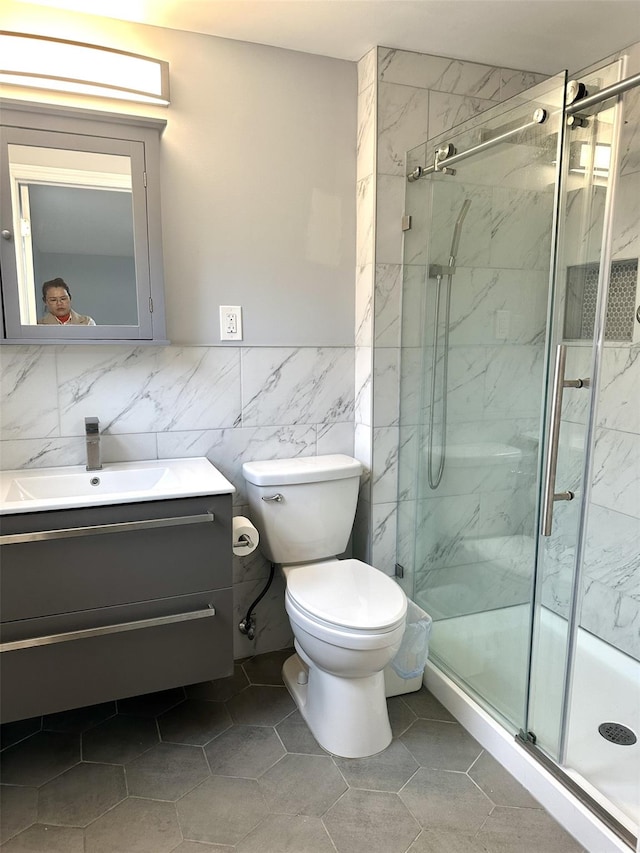 bathroom featuring toilet, walk in shower, tile patterned floors, vanity, and tile walls