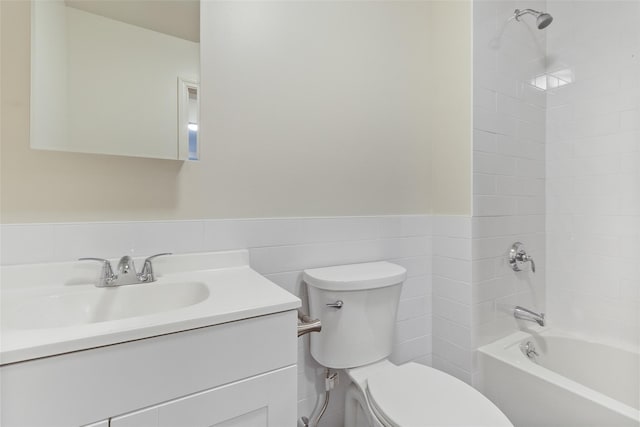 full bathroom featuring toilet, tiled shower / bath combo, vanity, and tile walls