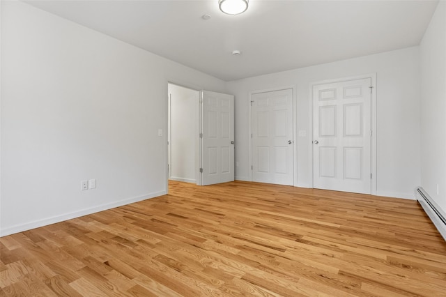 unfurnished bedroom featuring a baseboard heating unit and light hardwood / wood-style flooring