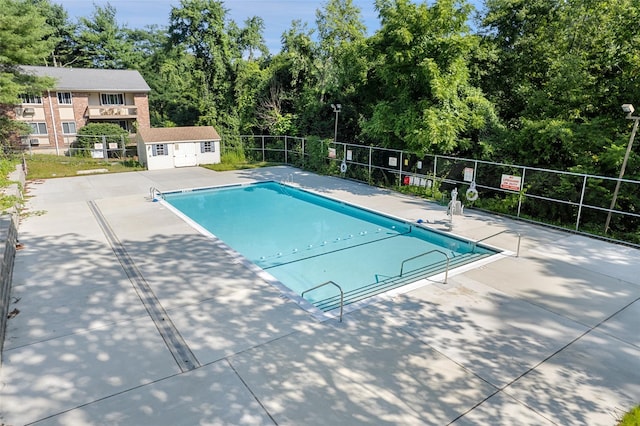 pool featuring a patio area, fence, and an outbuilding