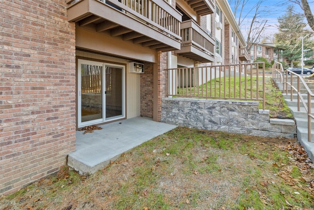 view of exterior entry featuring an AC wall unit, brick siding, fence, and a balcony