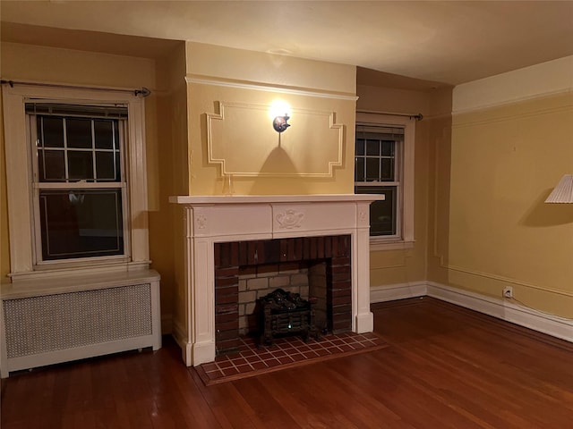 unfurnished living room featuring a brick fireplace, dark hardwood / wood-style floors, and radiator heating unit