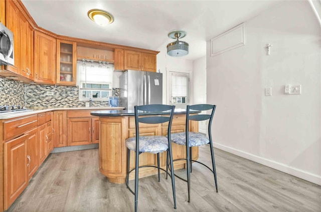 kitchen with appliances with stainless steel finishes, tasteful backsplash, a kitchen bar, a center island, and light wood-type flooring