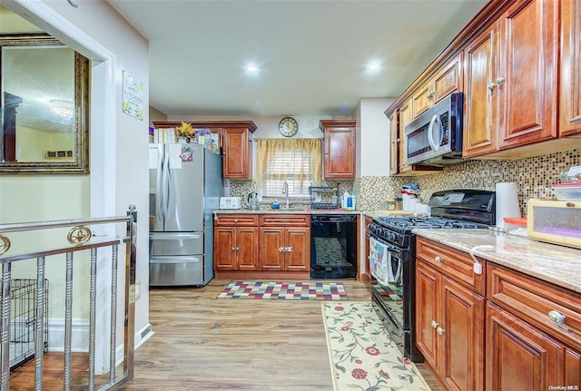 kitchen with black appliances, light hardwood / wood-style flooring, light stone counters, and decorative backsplash