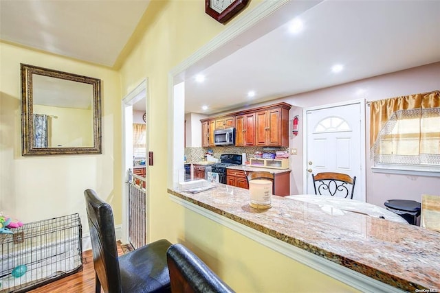 kitchen featuring light stone counters, kitchen peninsula, light hardwood / wood-style flooring, tasteful backsplash, and gas stove