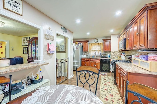 kitchen featuring backsplash, black appliances, light stone counters, and light hardwood / wood-style flooring