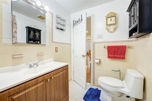 bathroom with toilet, tile patterned floors, vanity, and tile walls