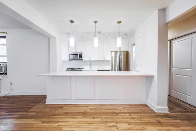 kitchen featuring white cabinets, light wood-type flooring, kitchen peninsula, pendant lighting, and appliances with stainless steel finishes