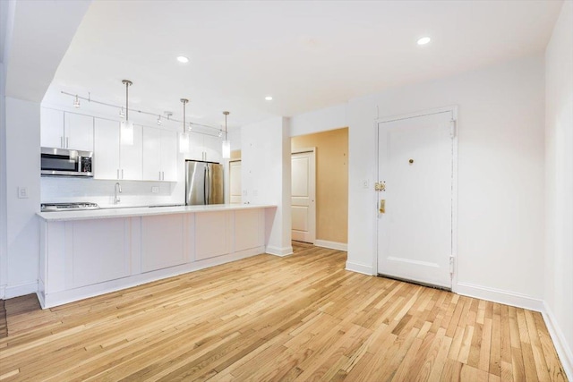 kitchen featuring appliances with stainless steel finishes, kitchen peninsula, pendant lighting, white cabinets, and tasteful backsplash