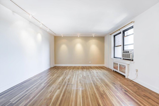 unfurnished room featuring light hardwood / wood-style floors, track lighting, cooling unit, and radiator