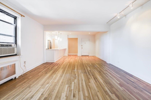 unfurnished living room with light wood-type flooring, track lighting, radiator heating unit, and cooling unit