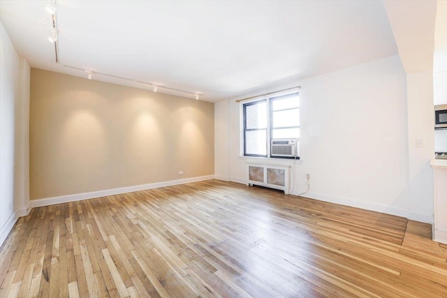 unfurnished room featuring cooling unit, light wood-type flooring, rail lighting, and radiator