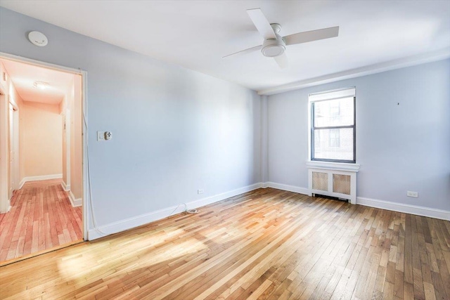 unfurnished room featuring ceiling fan, light hardwood / wood-style flooring, and radiator heating unit