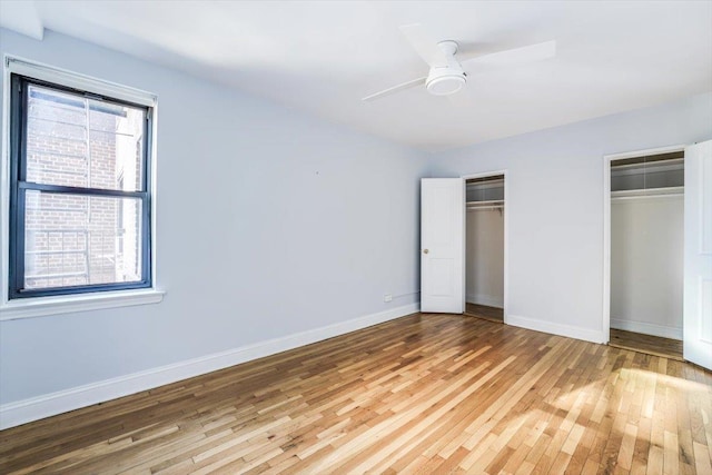 unfurnished bedroom with hardwood / wood-style flooring, two closets, ceiling fan, and multiple windows