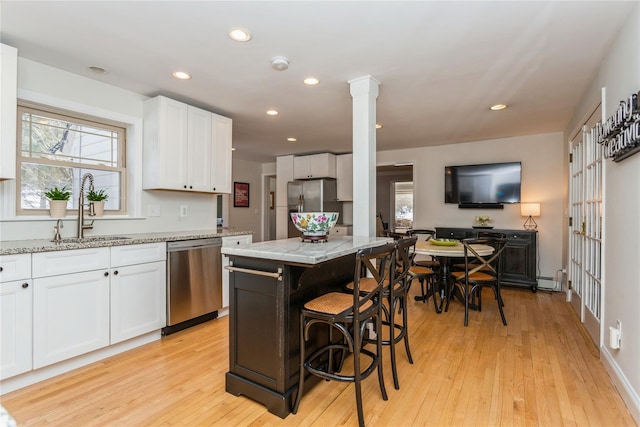 kitchen with sink, a kitchen island, stainless steel appliances, light stone countertops, and white cabinets